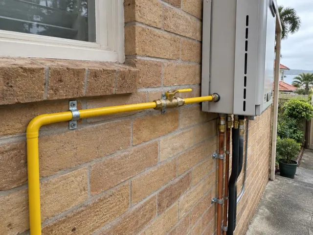 Outdoor gas pipe and wall-mounted gas unit beside a brick house exterior in Manly
